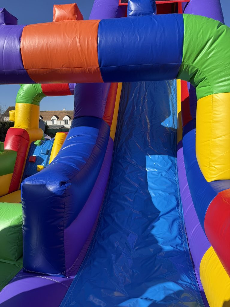 Enfant descendant le toboggan d’une structure gonflable LEGO avec sourire lors d’un anniversaire