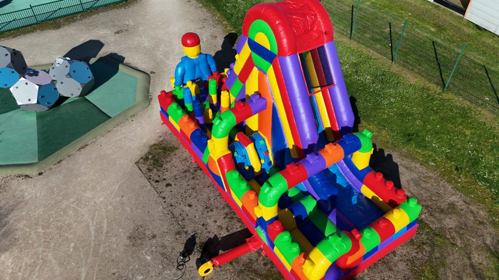 Enfants jouant en toute sécurité sur une structure gonflable LEGO avec filets de protection lors d’un anniversaire