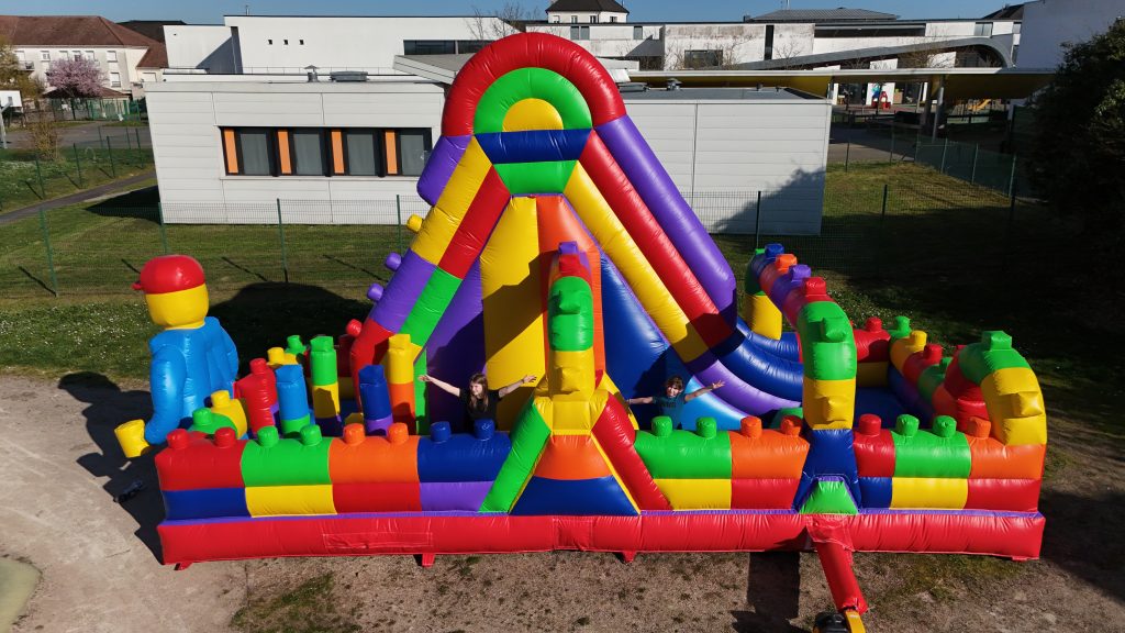 Structure gonflable LEGO géante installée en extérieur prête à accueillir des enfants pour un événement festif