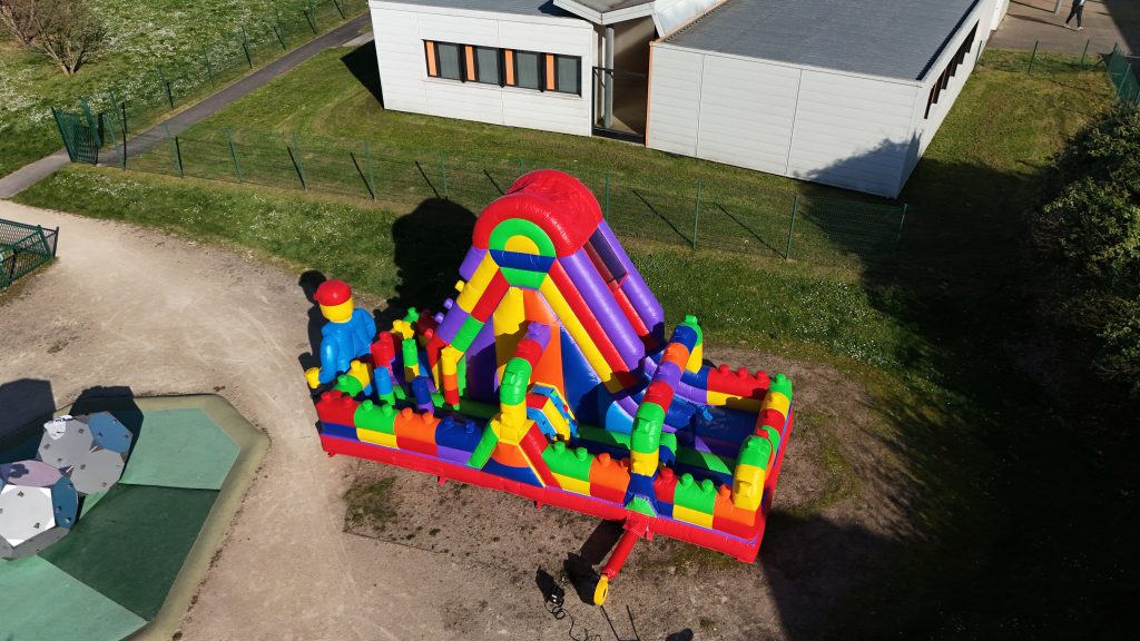 Structure gonflable LEGO géante pour enfants avec toboggan et briques colorées, idéale pour anniversaire et événement