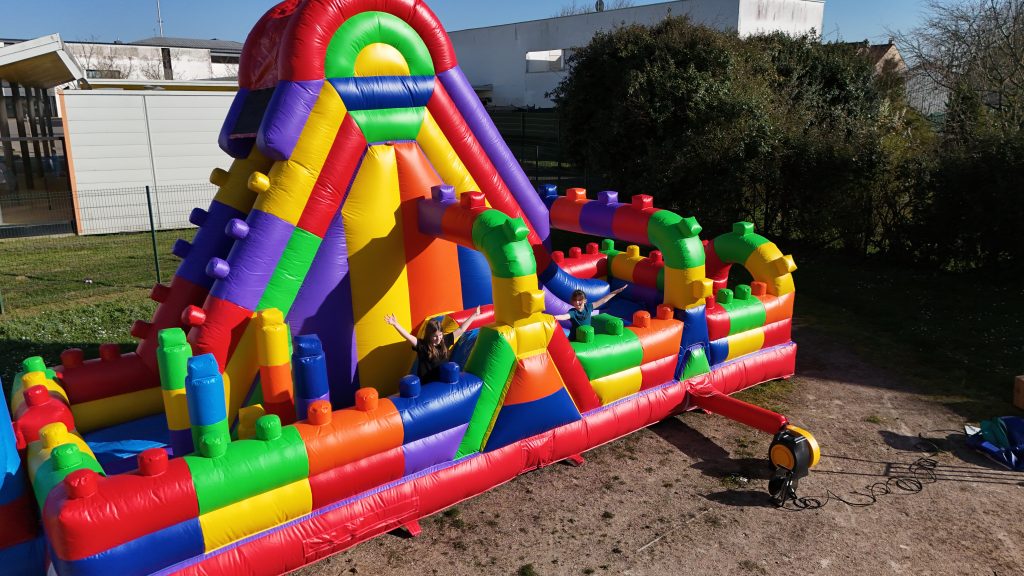 Enfants qui jouent sur une structure gonflable LEGO géante avec toboggan lors d’un anniversaire en extérieur
